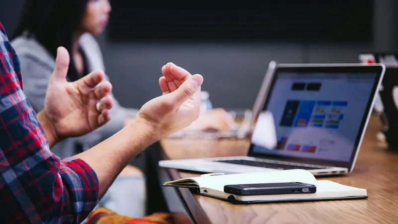 A person gesturing during a meeting with a laptop open on the table