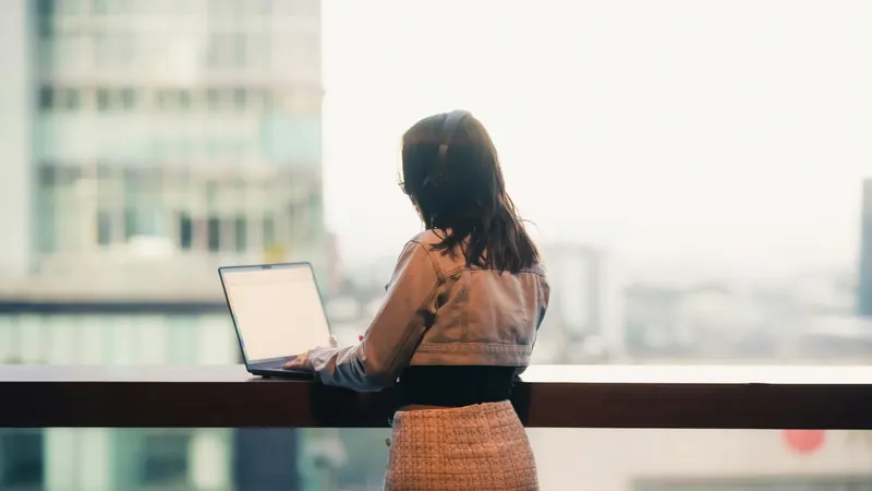 A woman working on a laptop at a window overlooking the city
